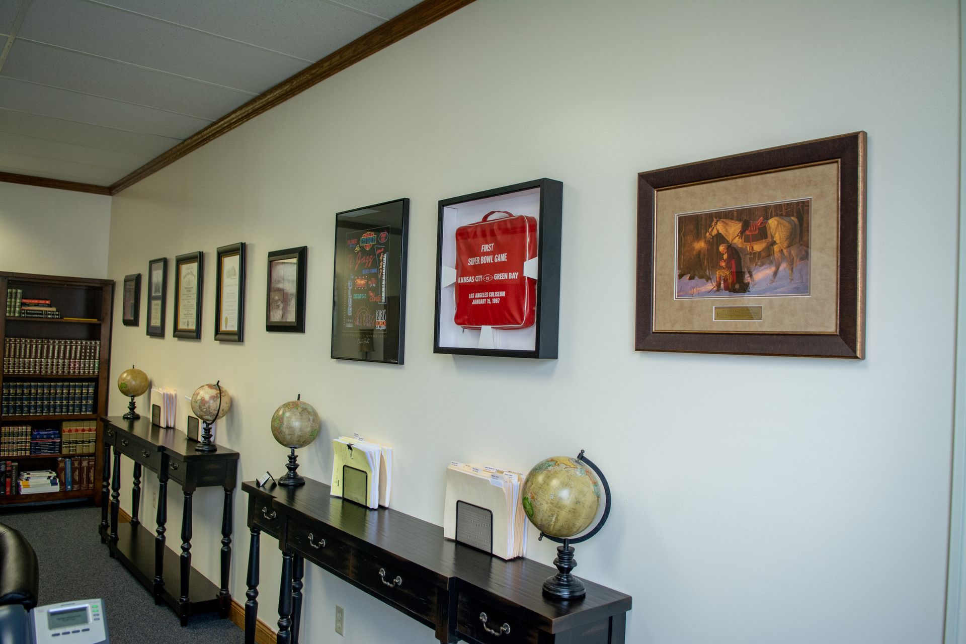 Office hallway with framed pictures and globes on a black shelf along a white wall