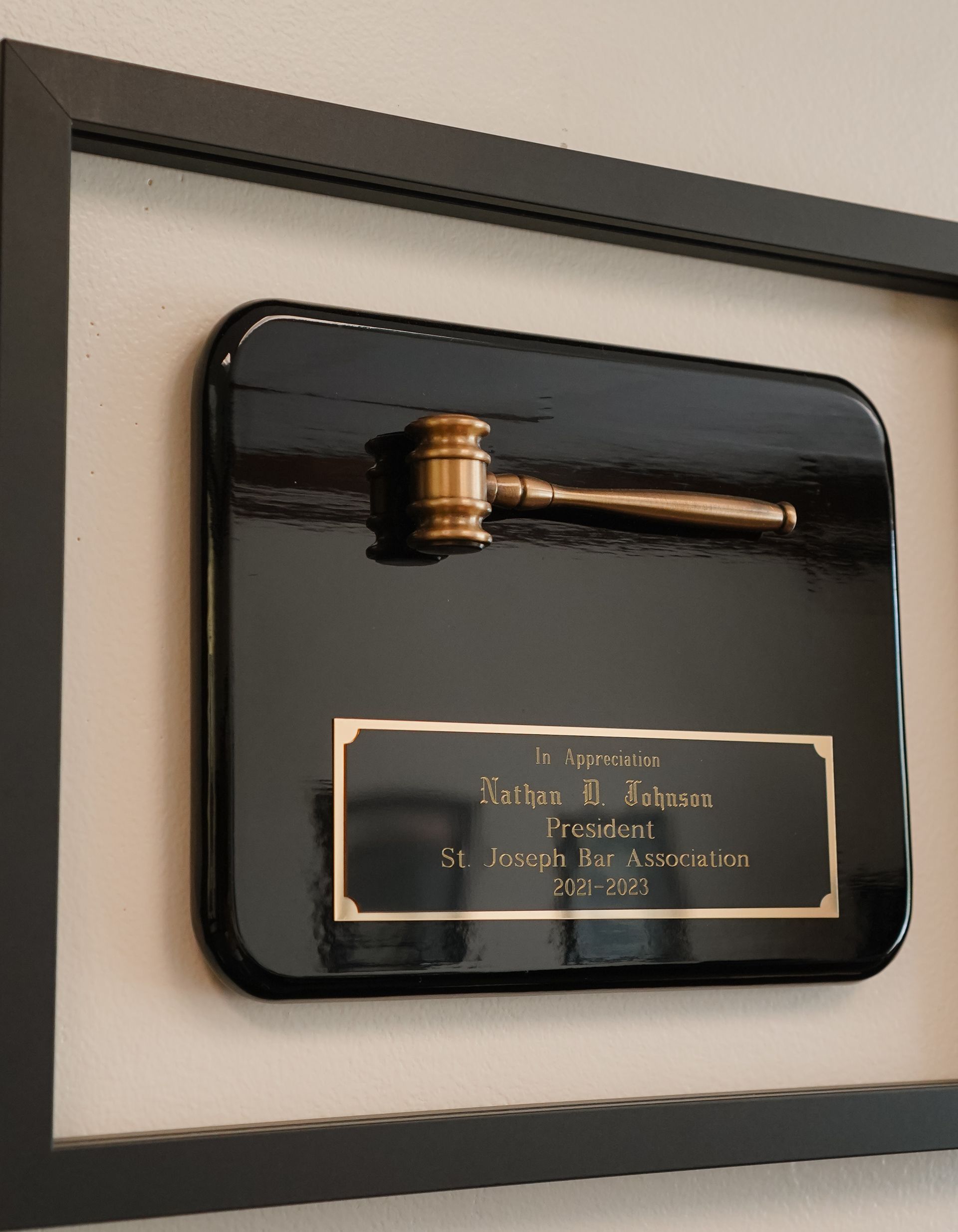 Framed black plaque with a gold gavel mounted on a wall, likely commemorating a legal or judicial event
