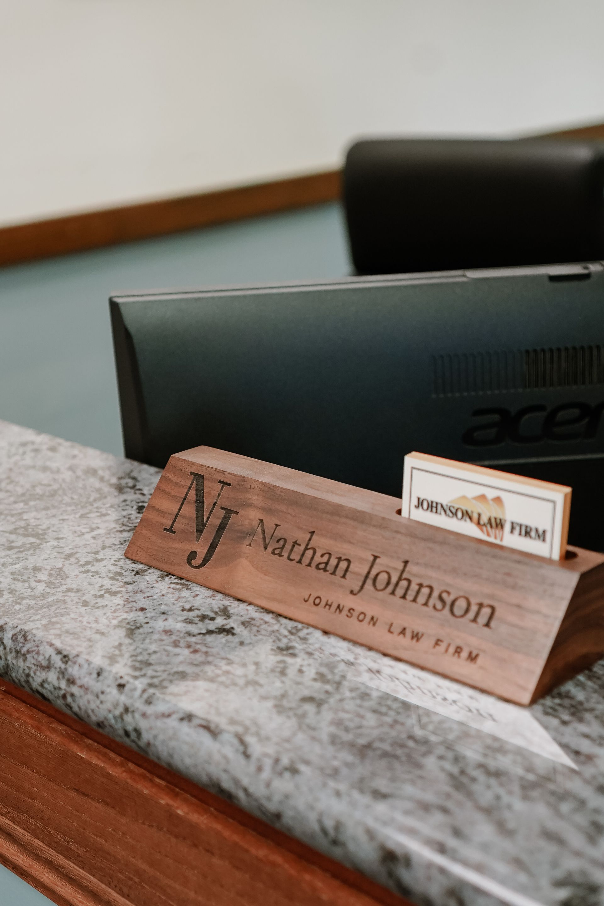Wooden desk nameplate reading “Jonathan Johnson” in front of an Acer laptop and a small desk sign.