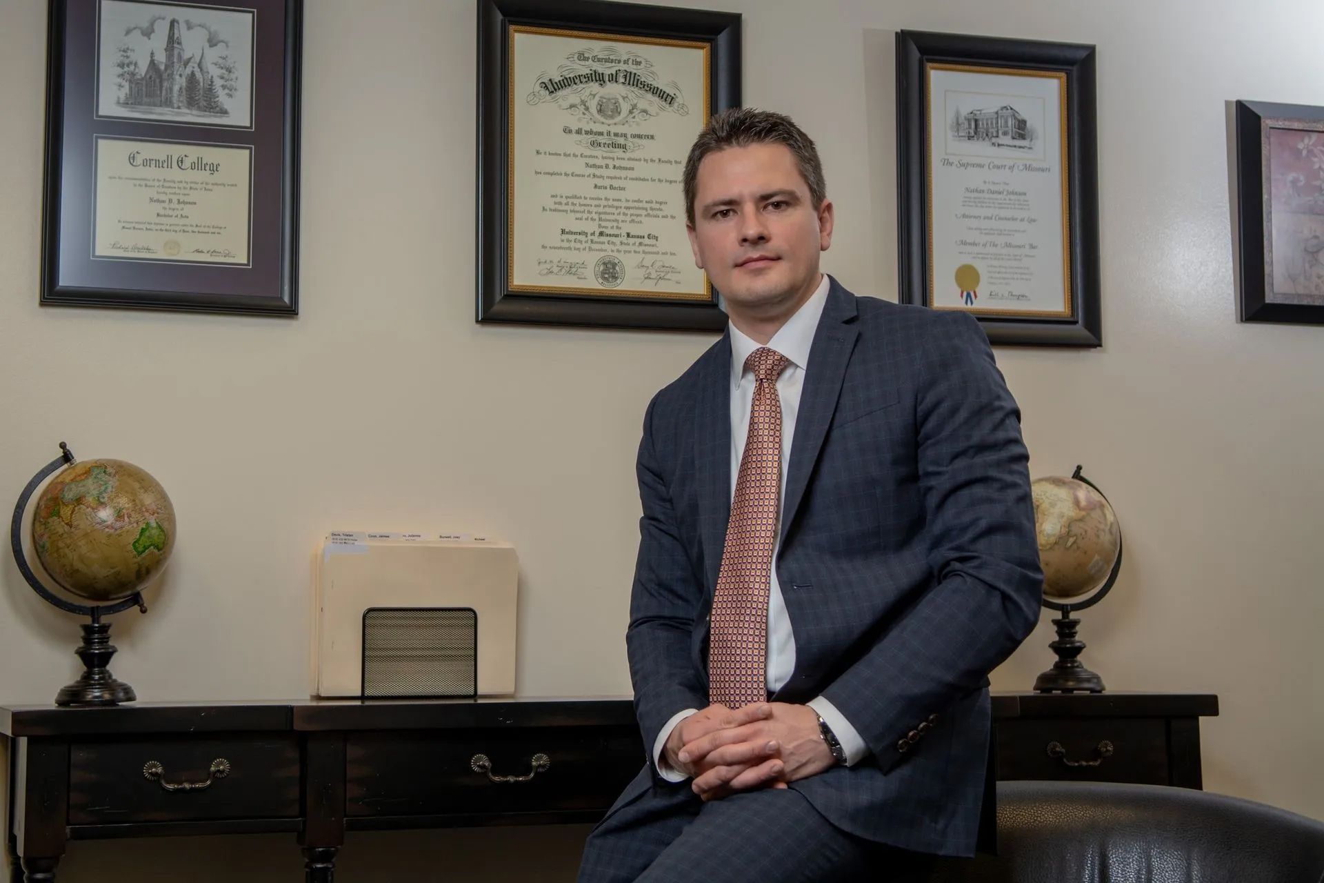 Man sitting in an office with framed certificates and globe decor behind him.