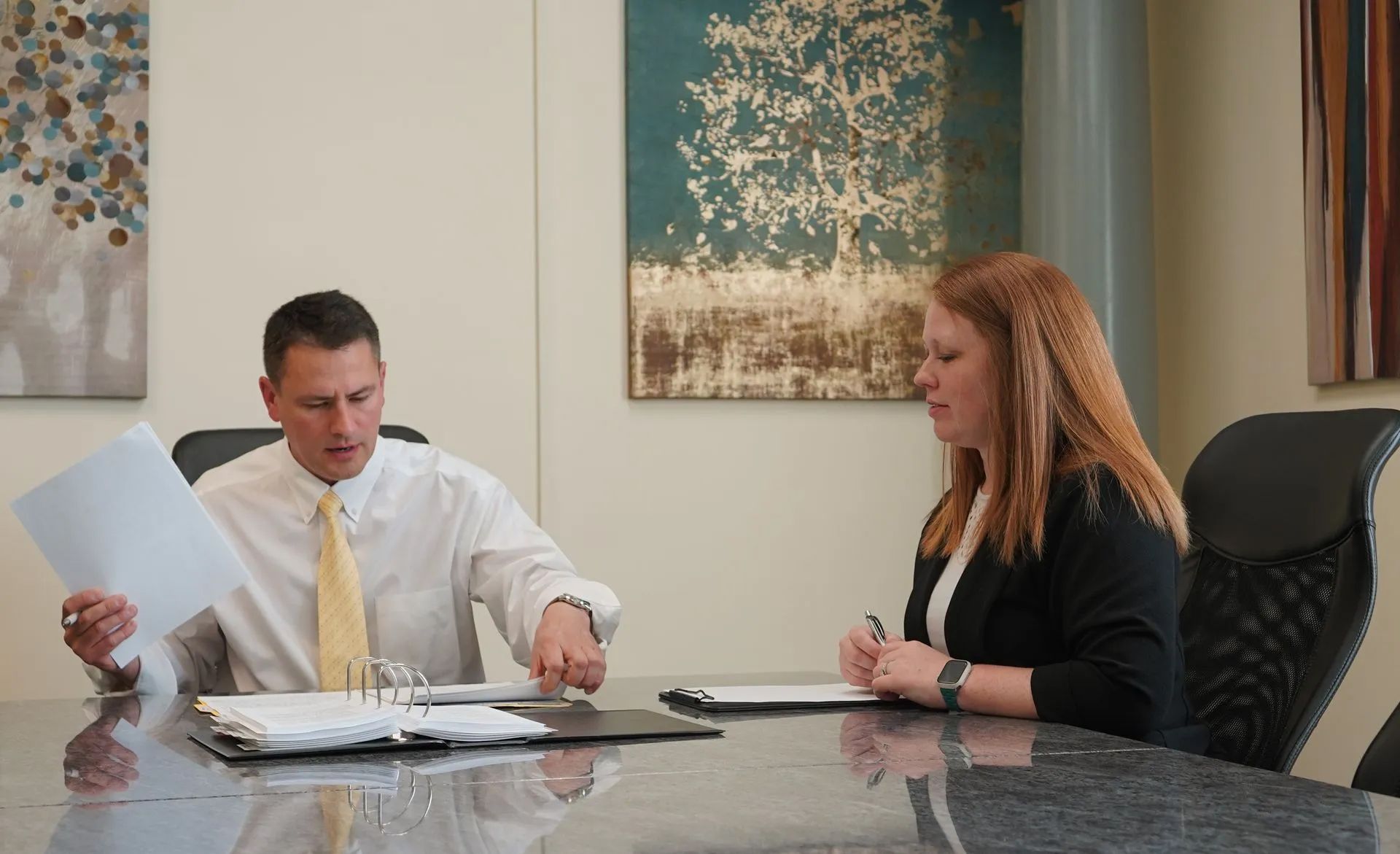 Two people in an office reviewing documents at a conference table, one pointing at papers.