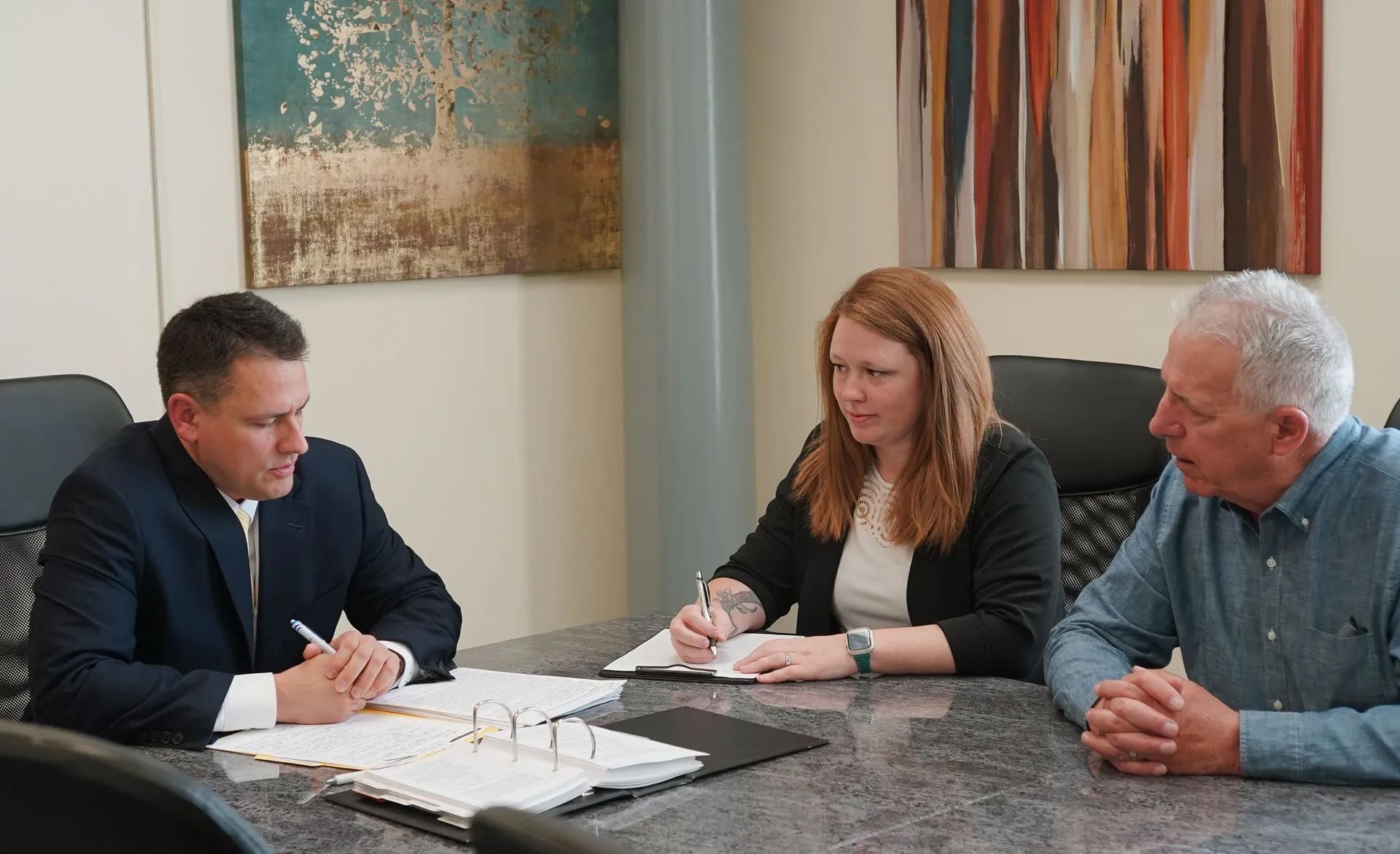 Three people in a conference room reviewing documents at a table