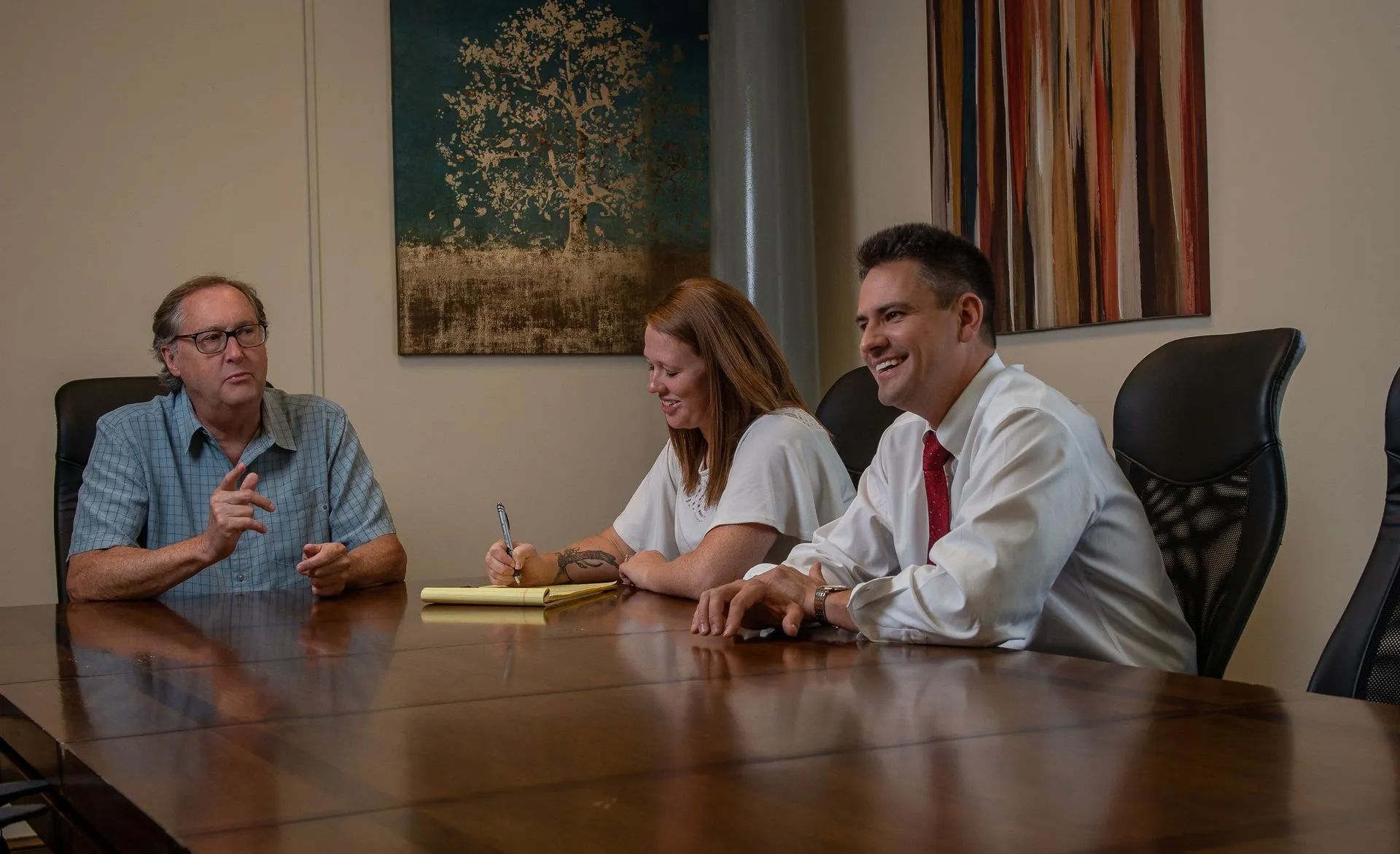 Three people seated at a conference table in an office, smiling and talking.