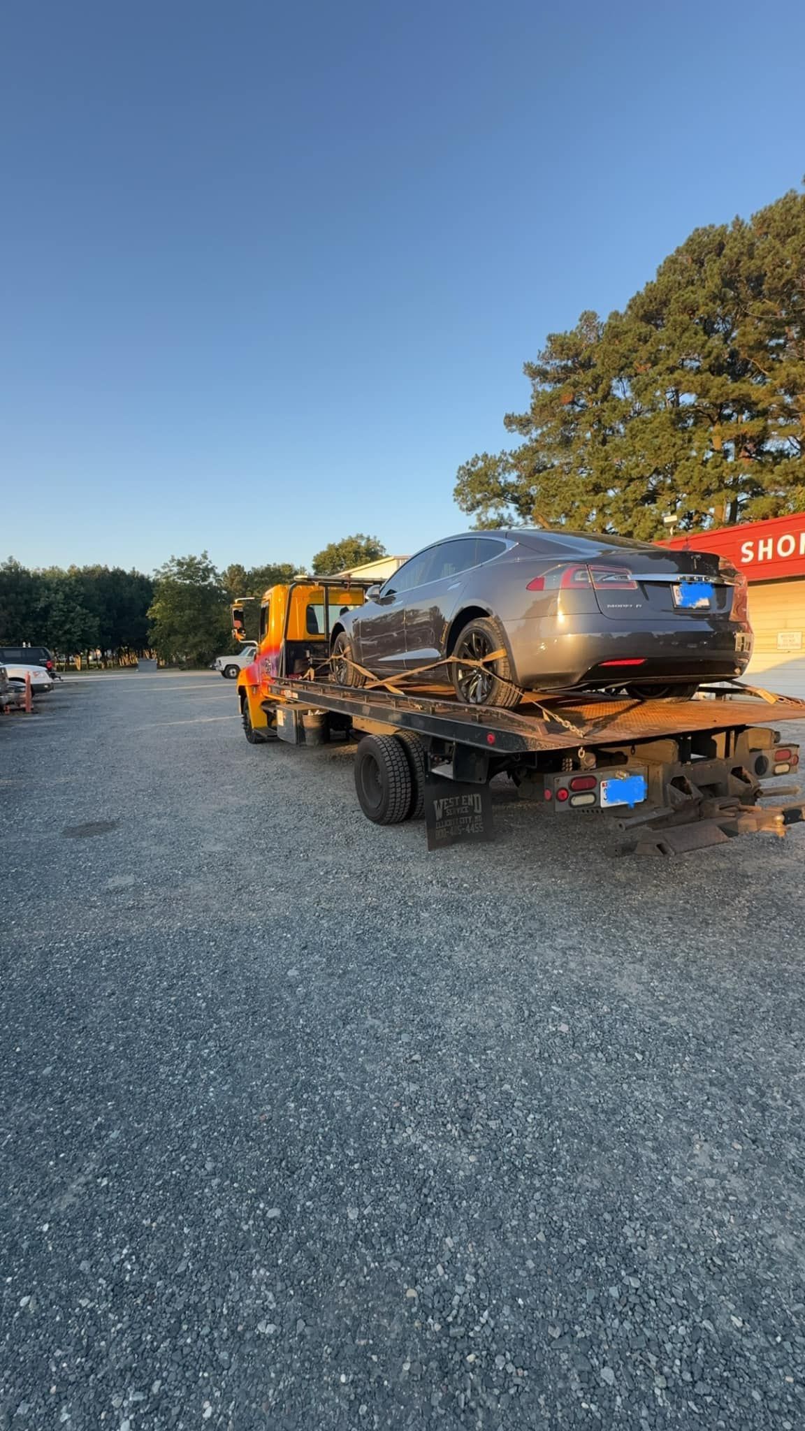 A car is being towed by a tow truck in a gravel lot.