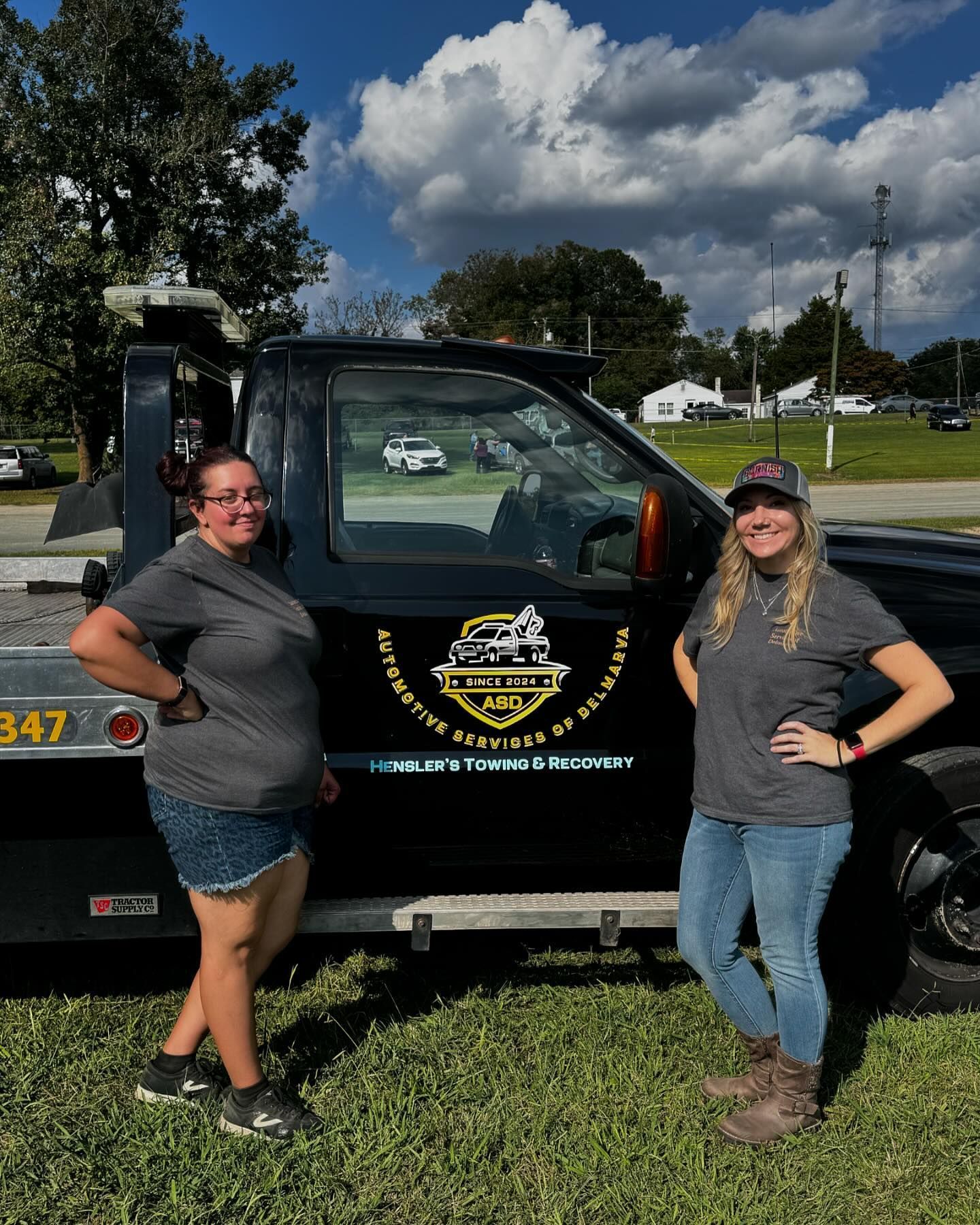 Two women are standing in front of a tow truck.