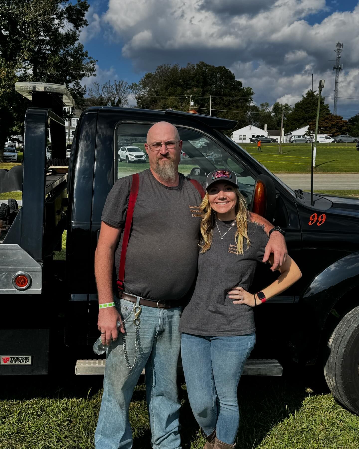 A man and a woman are standing in front of a tow truck.