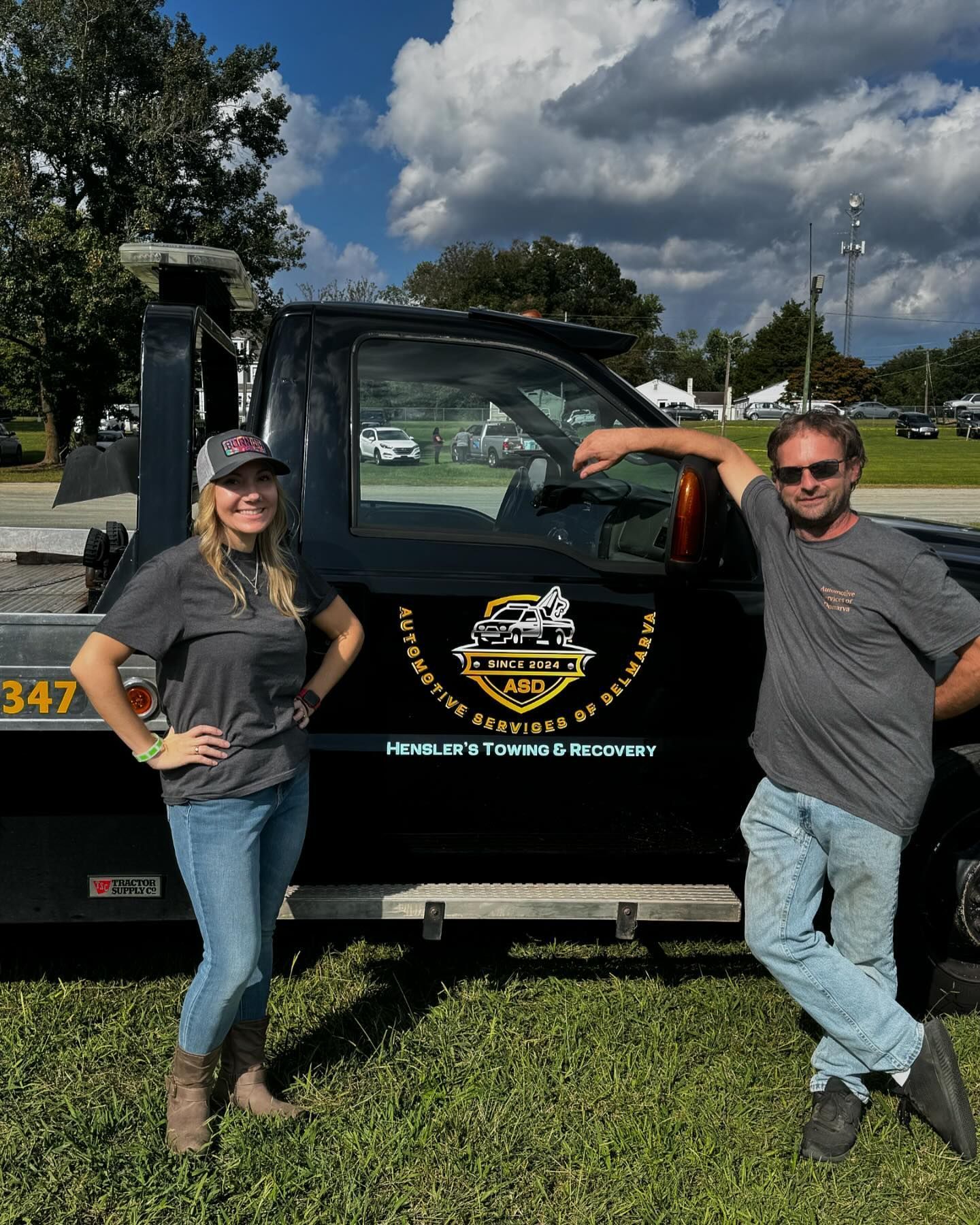 A man and a woman are standing in front of a tow truck.