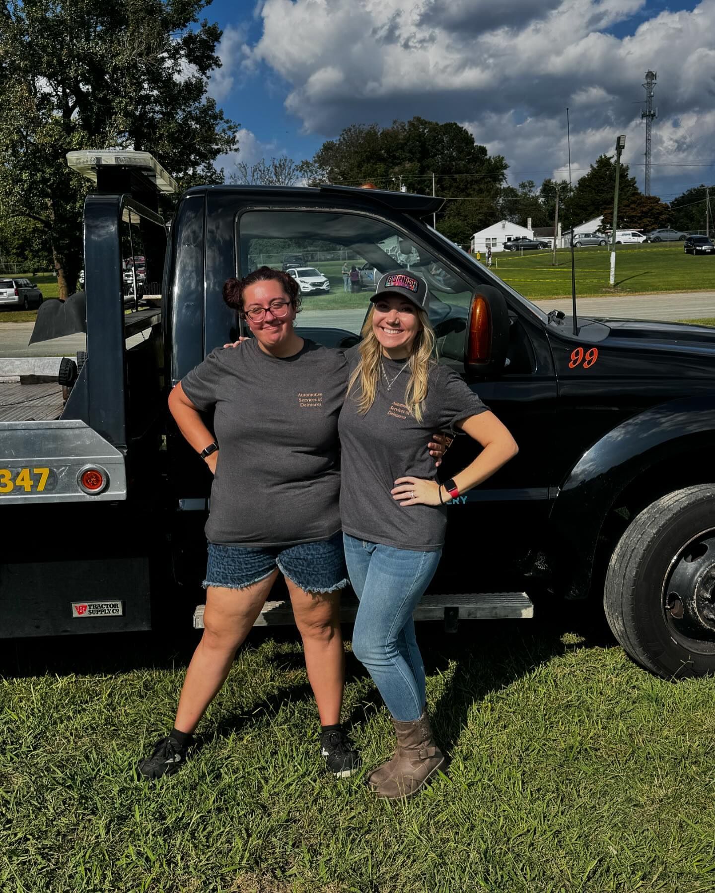 Two women are posing for a picture in front of a tow truck.
