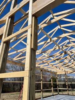 A low-angle view of a wooden post-and-beam building frame under a clear blue sky. 