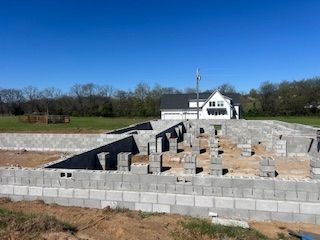 A concrete block foundation for a new house under construction on a sunny day, with a finished house in the distance. 