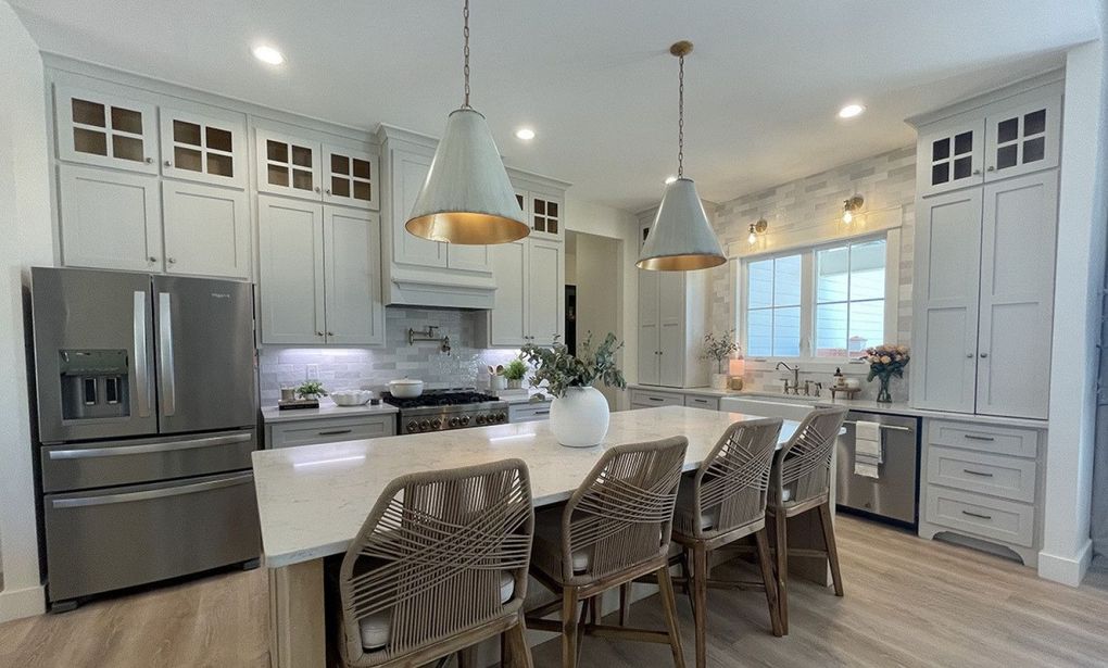 A kitchen with white cabinets , stainless steel appliances , a large island with a table and chairs.
