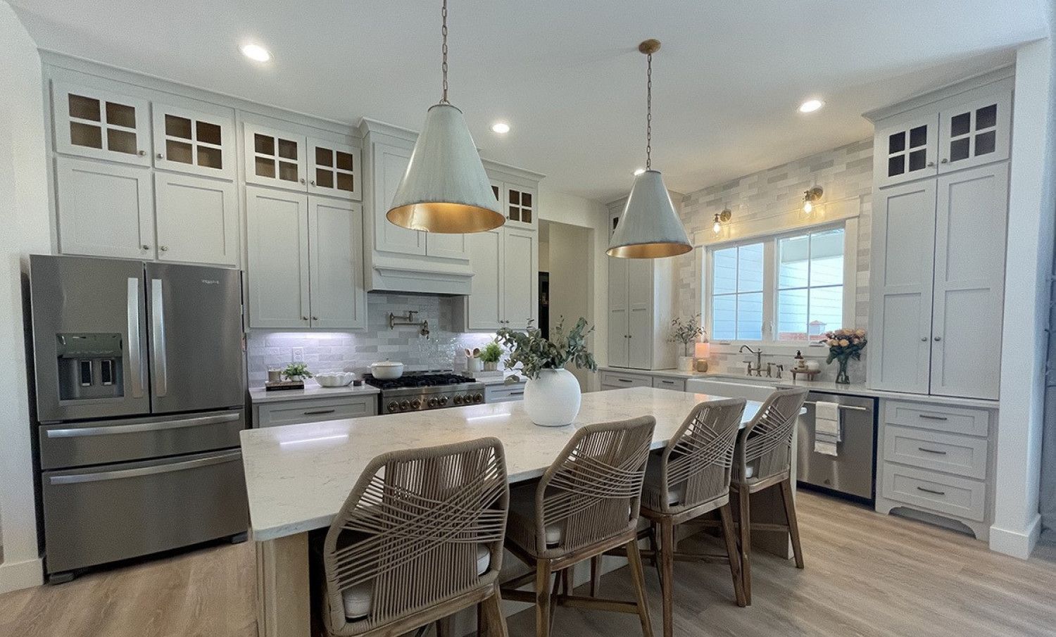 A kitchen with white cabinets , stainless steel appliances , a large island with a table and chairs.