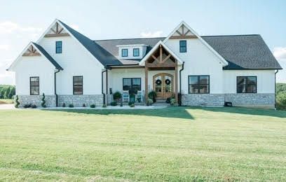White farmhouse with stone accents, wooden accents, and a green lawn.