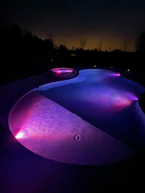 Nighttime view of a pool illuminated with purple and pink lights.