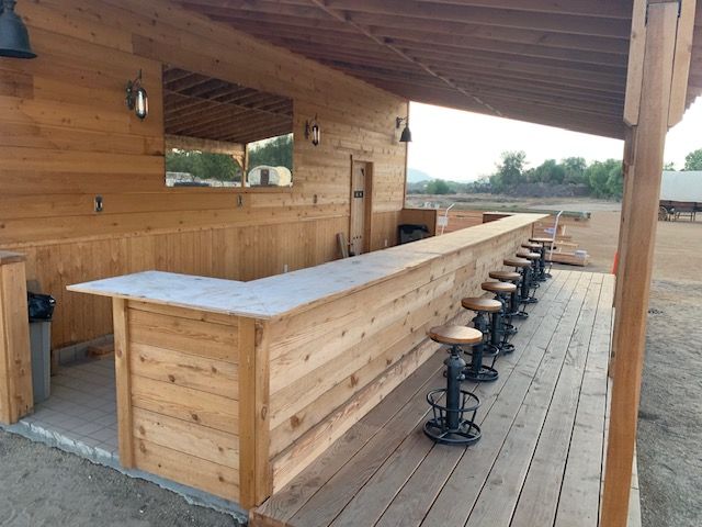 Outdoor wooden bar with stools and a covered roof.
