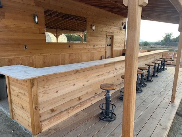Outdoor bar with wood paneling, counter, and stools under a wooden roof.