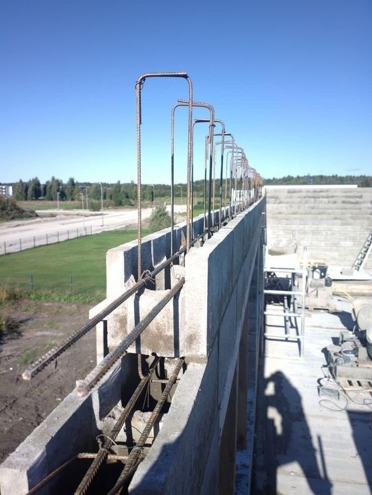 Concrete wall under construction with steel rebar extending upward, blue sky.
