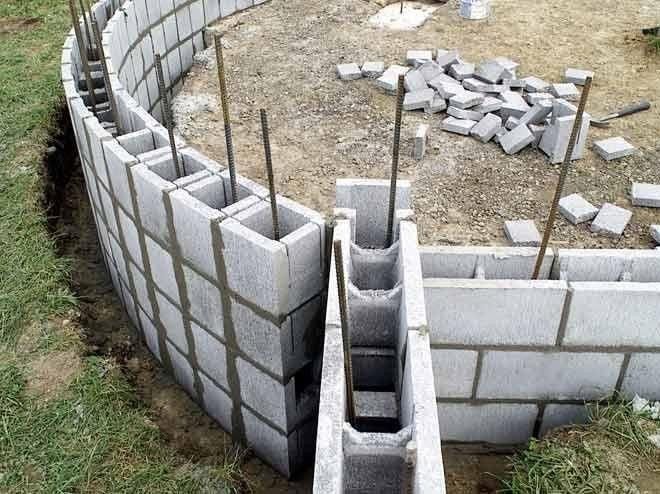 Curved cinder block wall under construction with rebar supports and mortar.