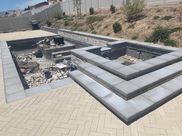 Construction site with a partially built pool and patio area with gray concrete blocks.