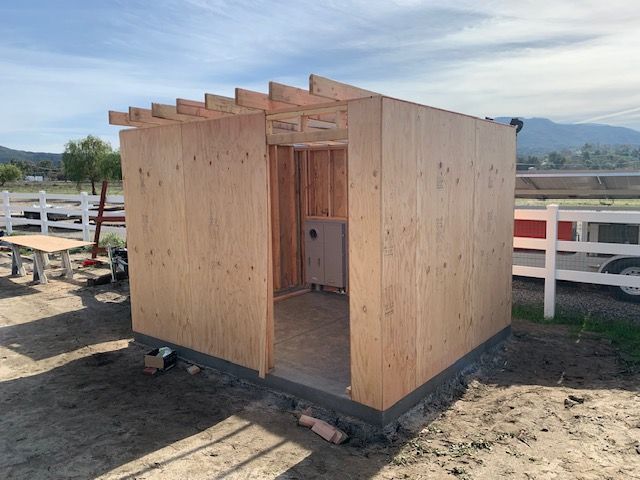 Wooden shed under construction outdoors with a partial roof.