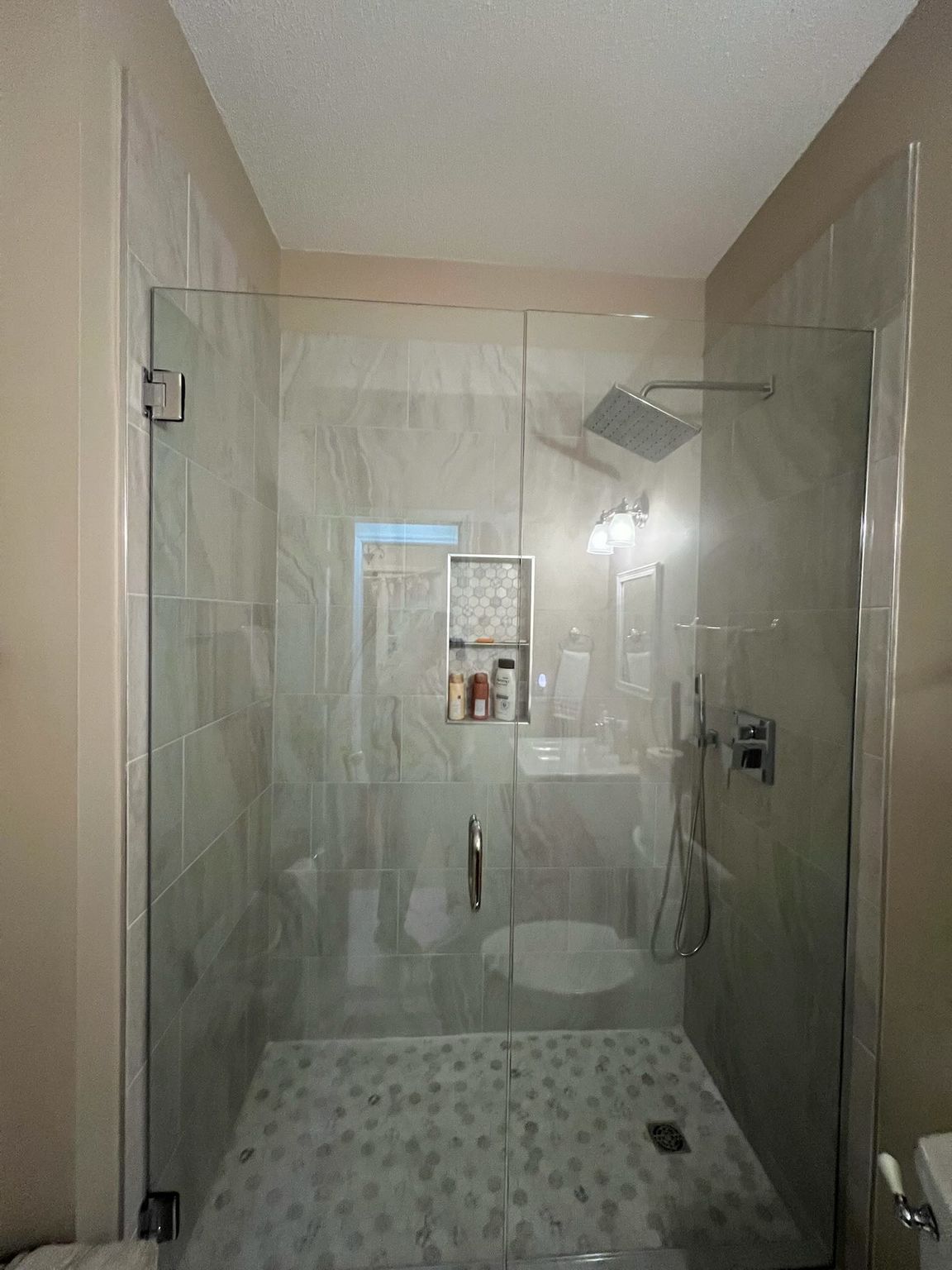 Glass shower enclosure in a bathroom with tiled walls and a pebble floor.