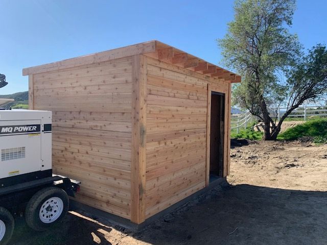Wooden shed with open doorway and power generator in a sunny outdoor setting.