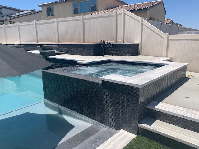 Pool and spa with dark tile and white fence in a backyard setting.
