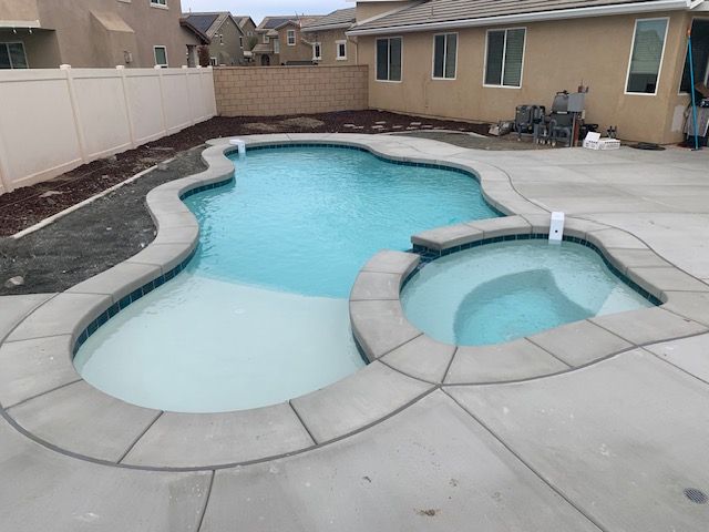 A newly constructed swimming pool and spa with light blue water and a gray concrete surround.