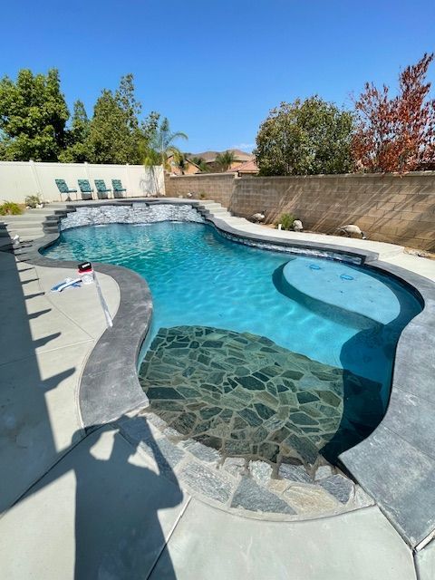 A swimming pool with clear blue water and a dark grey stone bottom, on a sunny day.