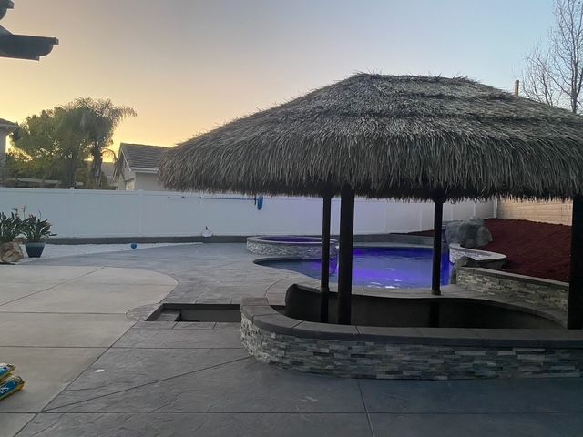 Poolside tiki hut with thatched roof, concrete patio, and spa. Evening sky.