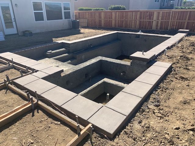 Pool under construction; concrete shell with steps and surrounding borders in a backyard setting.