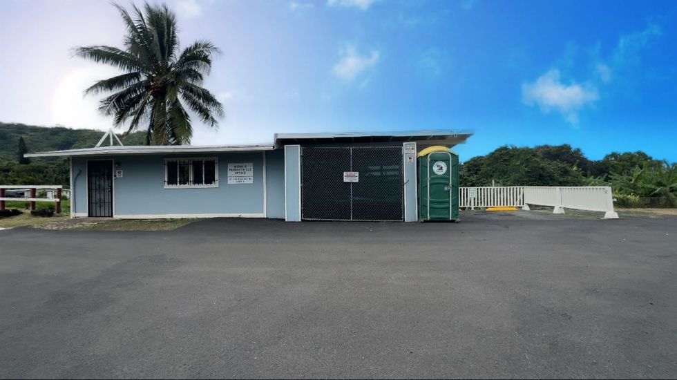 Blue building with black gate and palm tree against a cloudy sky.