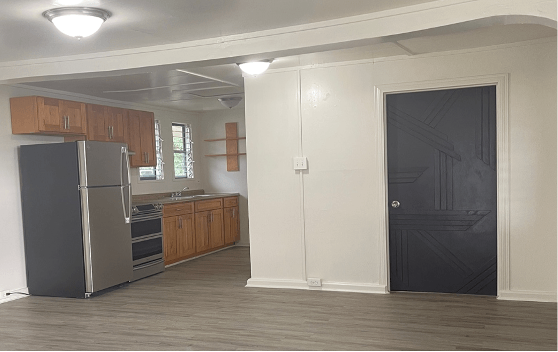 An open-concept kitchen and living space. The kitchen has light wood cabinets, stainless appliances, and a black door.