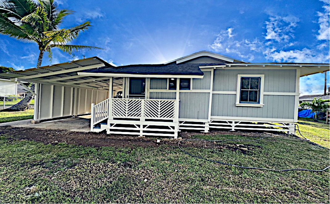 Light blue house with white trim, a carport, and a porch, under a bright sky.