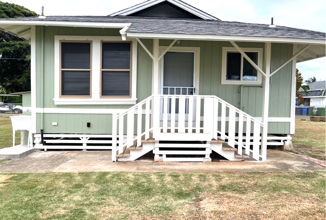 Green house with white trim and porch; grass lawn.