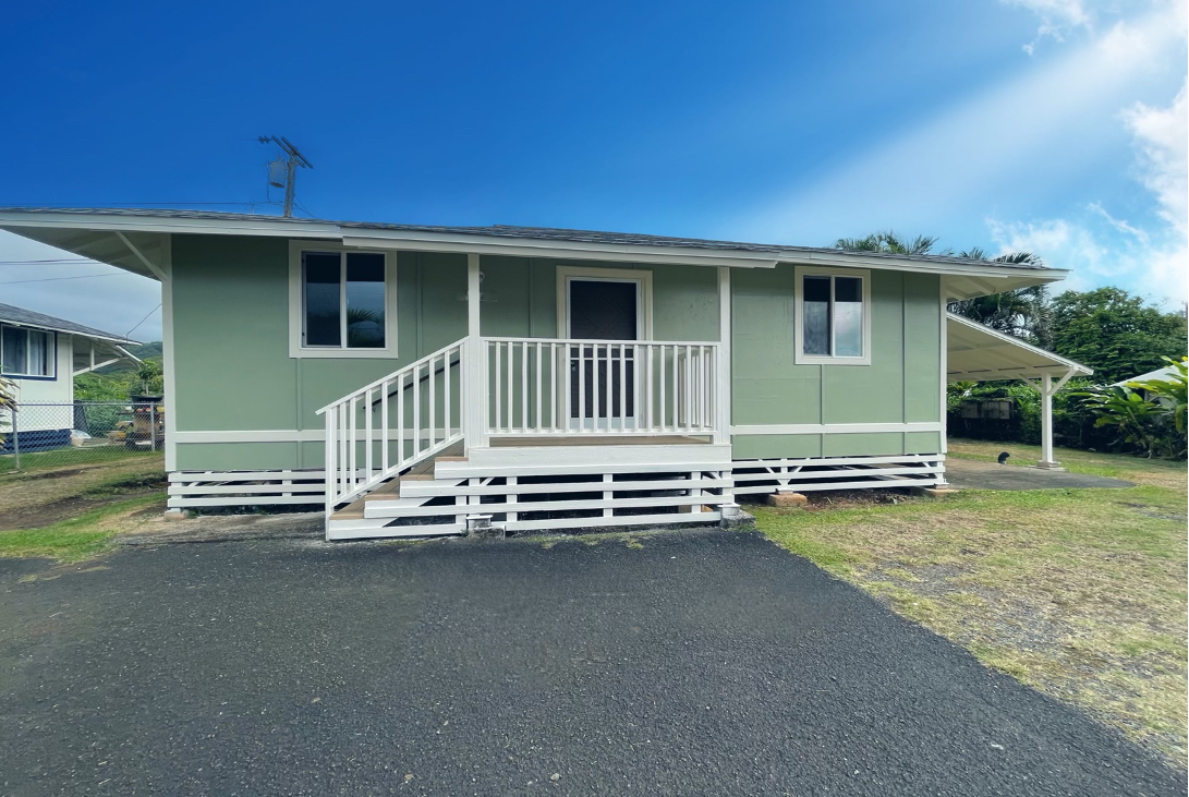 Green house with white trim and porch, asphalt driveway, blue sky.