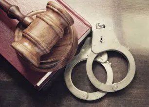 Wooden gavel and handcuffs rest on a closed law book.