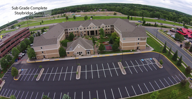 Aerial view of a large beige building with a mostly empty parking lot and surrounding trees.