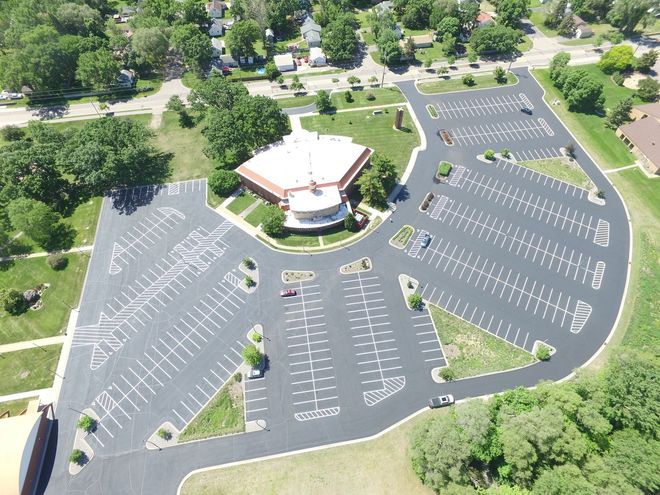 Aerial view of a large empty parking lot surrounding a central building with trees and roads nearby