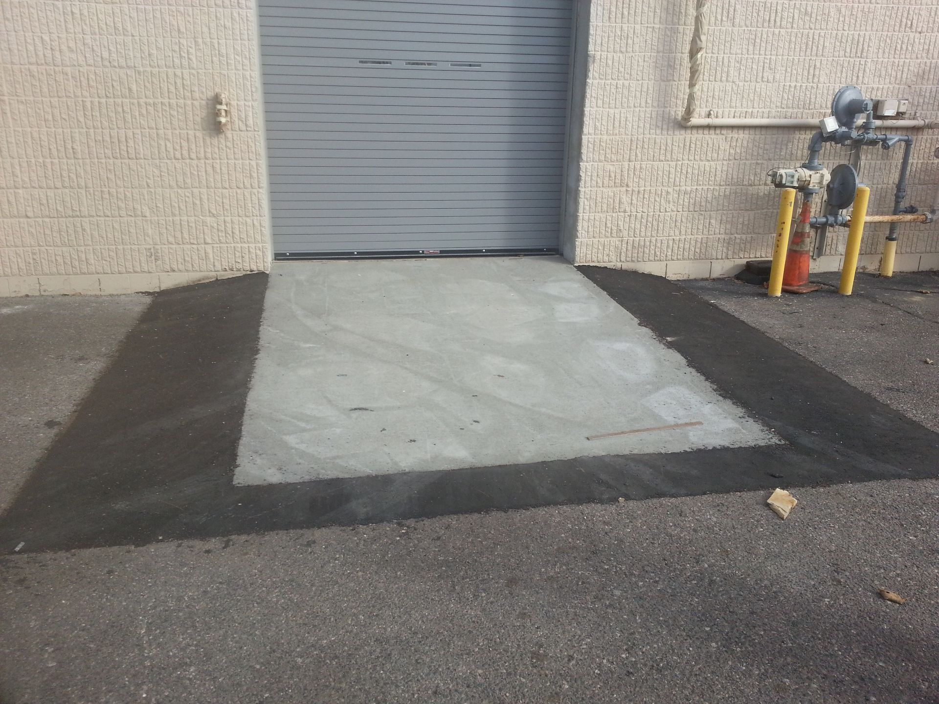 Concrete loading ramp before a gray roll-up door, with yellow safety bollards on the right.