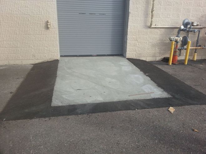 Concrete loading ramp before a gray roll-up door, with yellow safety bollards on the right.