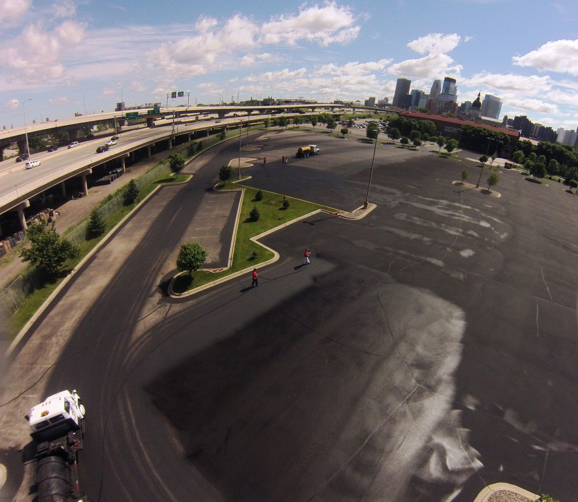 Wide aerial view of an empty parking lot beside a highway, with city skyline in the distance