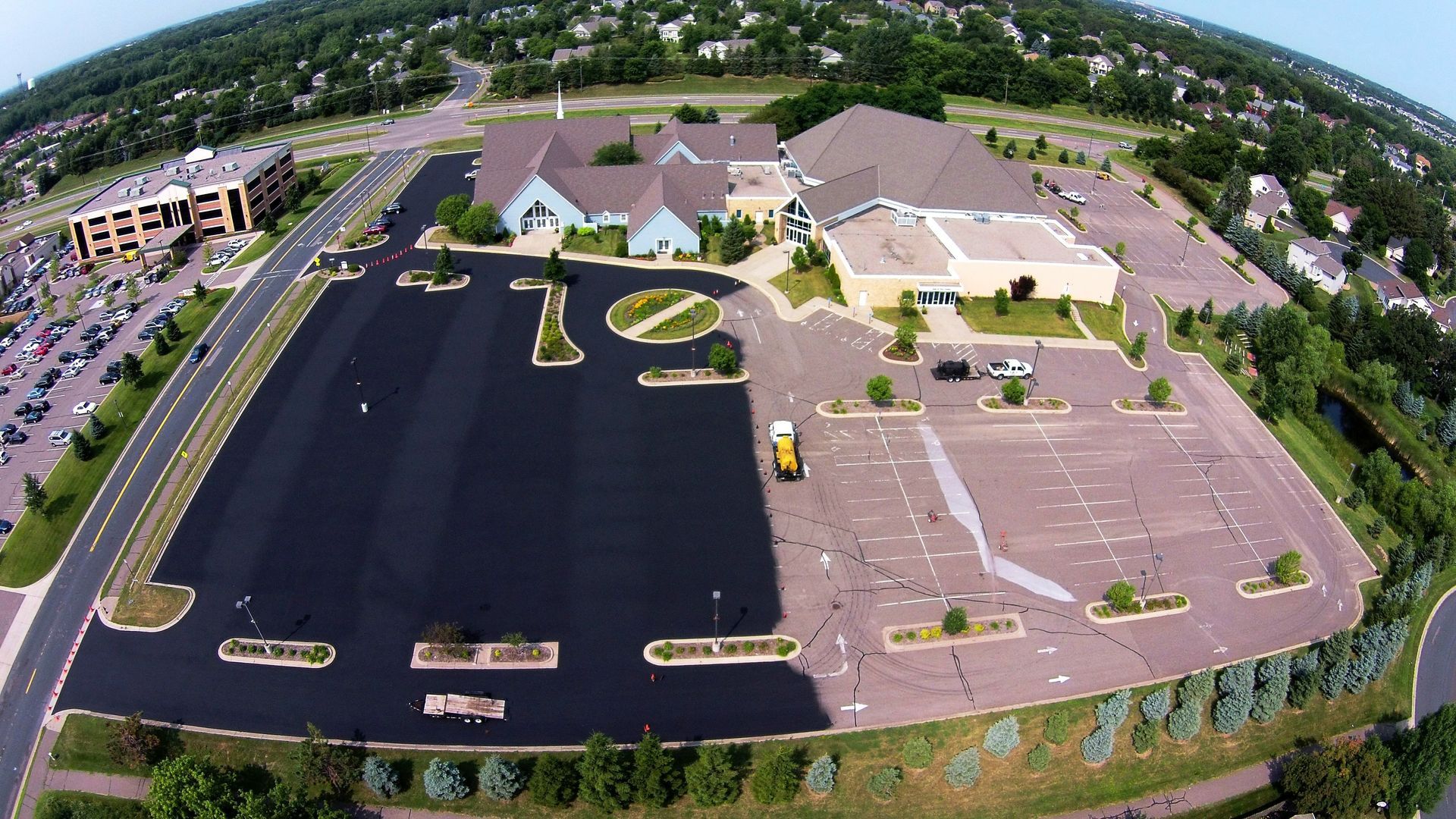 Aerial view of a church and office complex with large parking lots and surrounding trees.