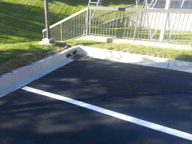 Parking lot with painted white lines beside a white railing and grassy slope in sunlight