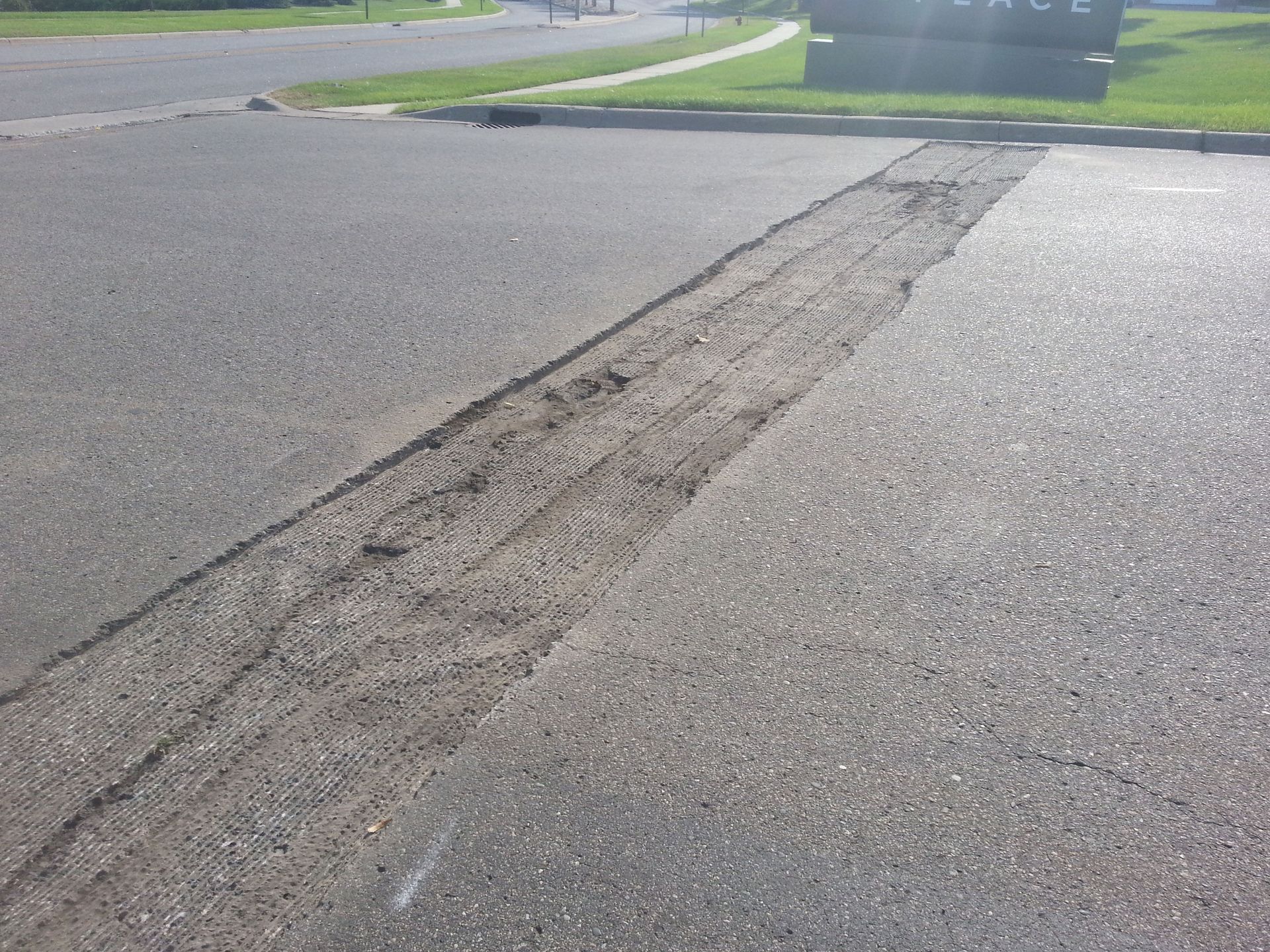 Cracked asphalt road with a long repaired seam near a grassy curb
