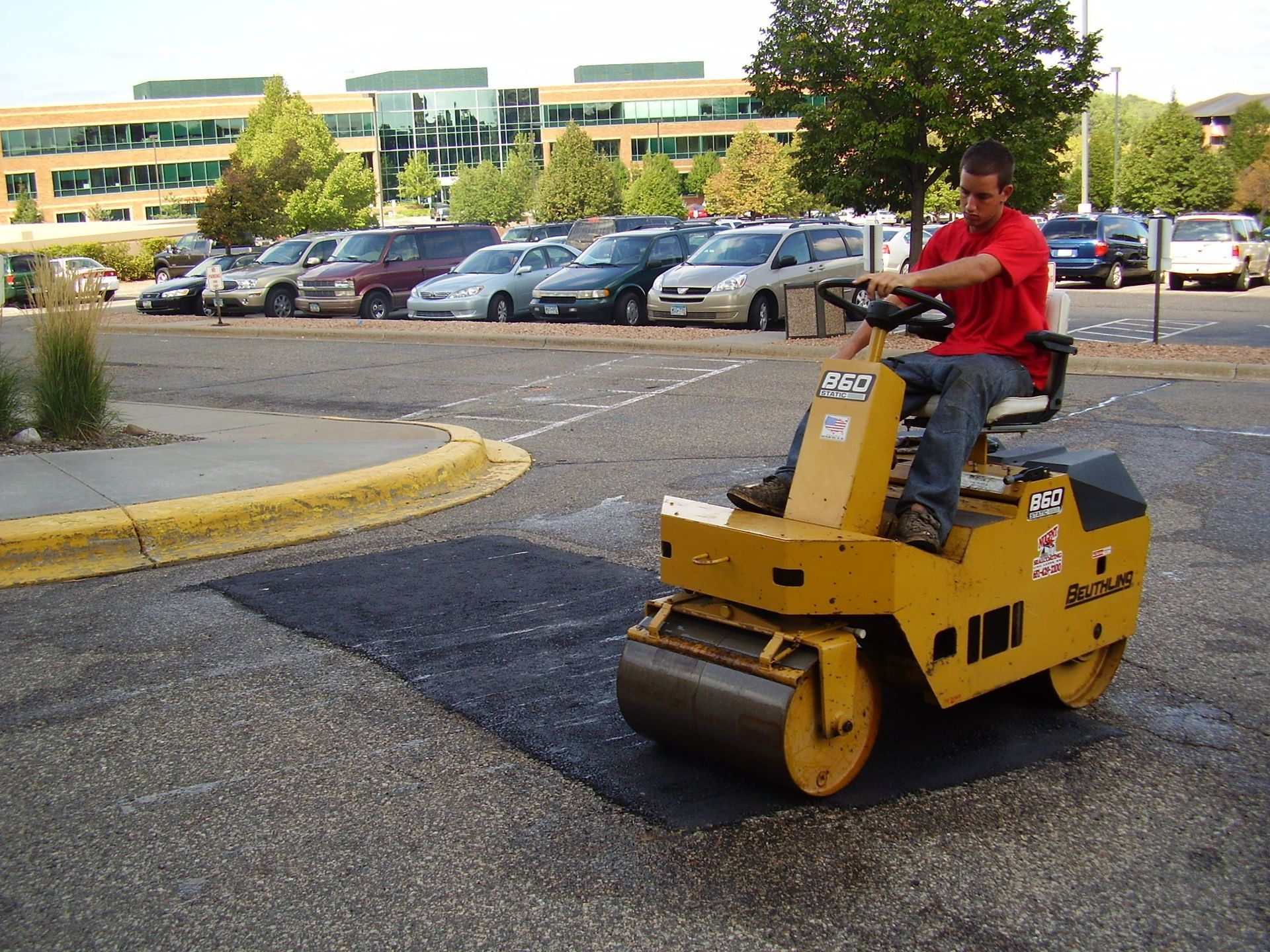 Worker driving a yellow road roller on a parking lot pavement repair site