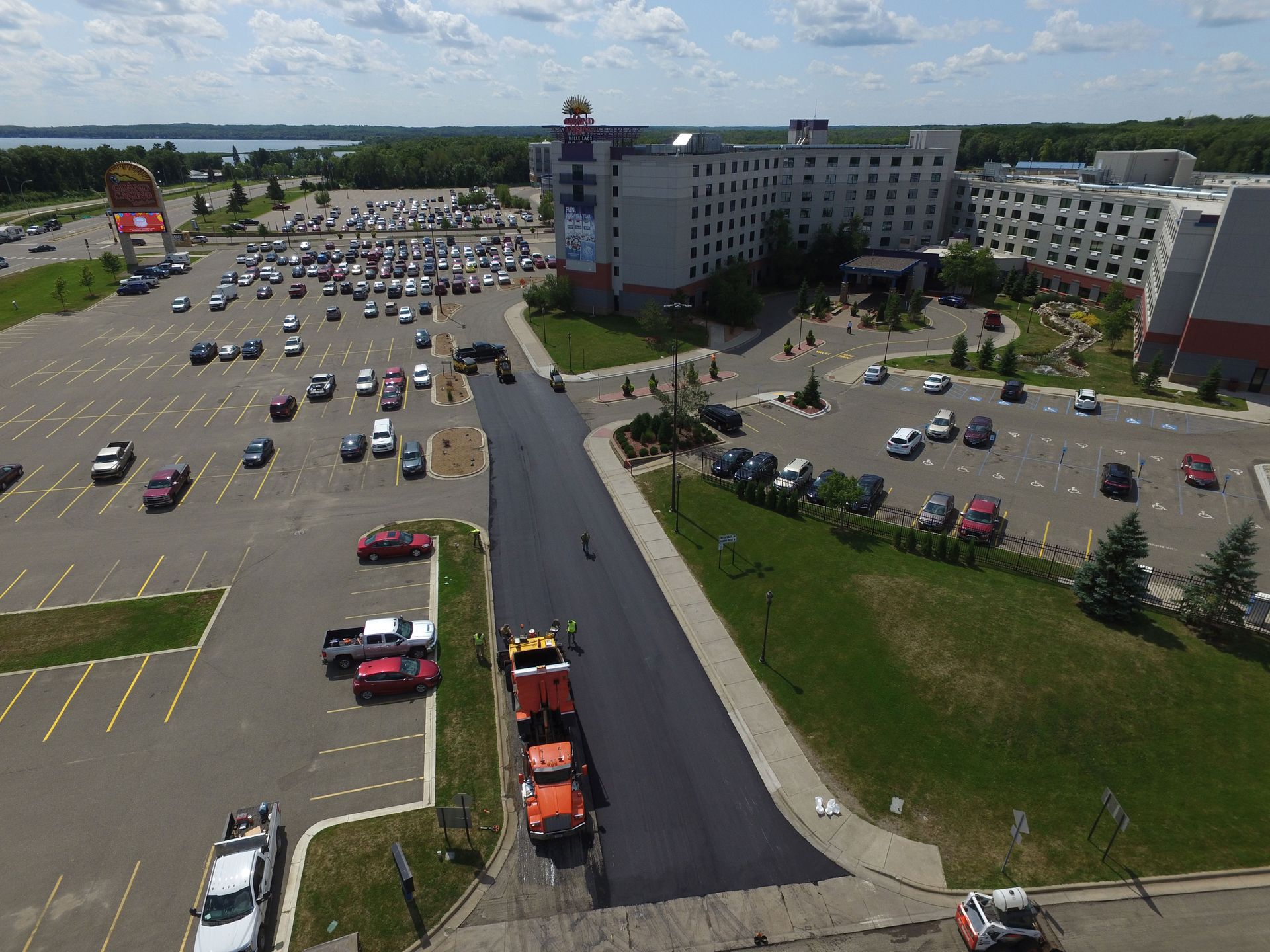 Aerial view of a large parking lot beside a hotel, with many cars and a road leading to the entrance.