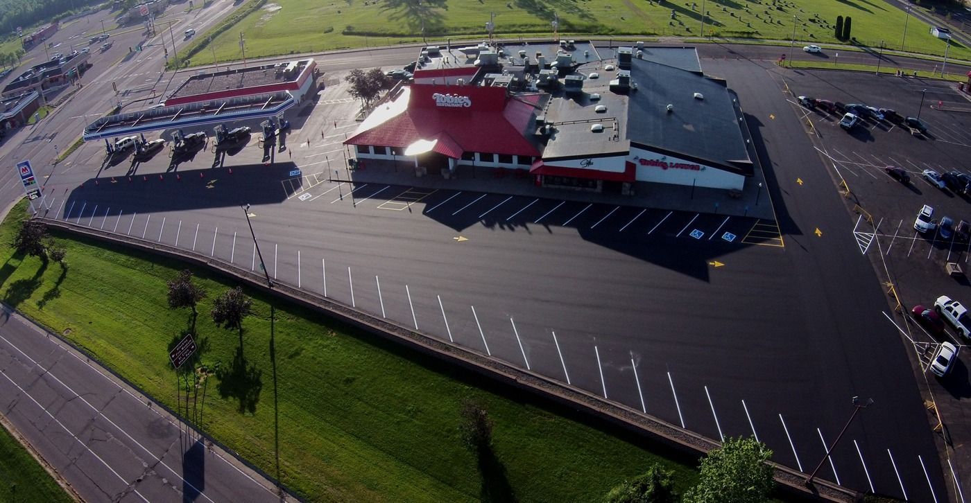 Aerial view of a large commercial building with a mostly empty parking lot and grassy surroundings.