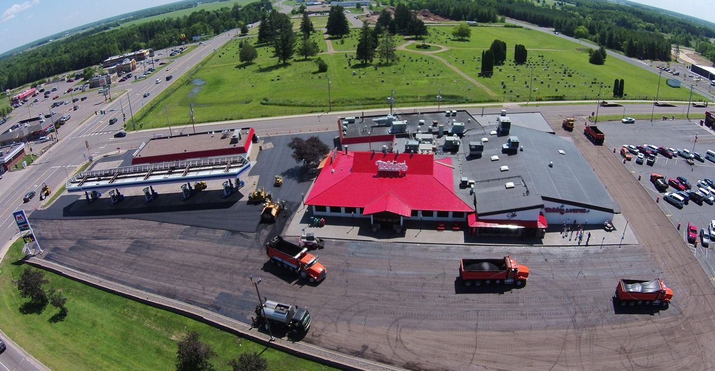 Aerial view of a truck stop with a red-roofed building, parked trucks, and surrounding grassy fields.
