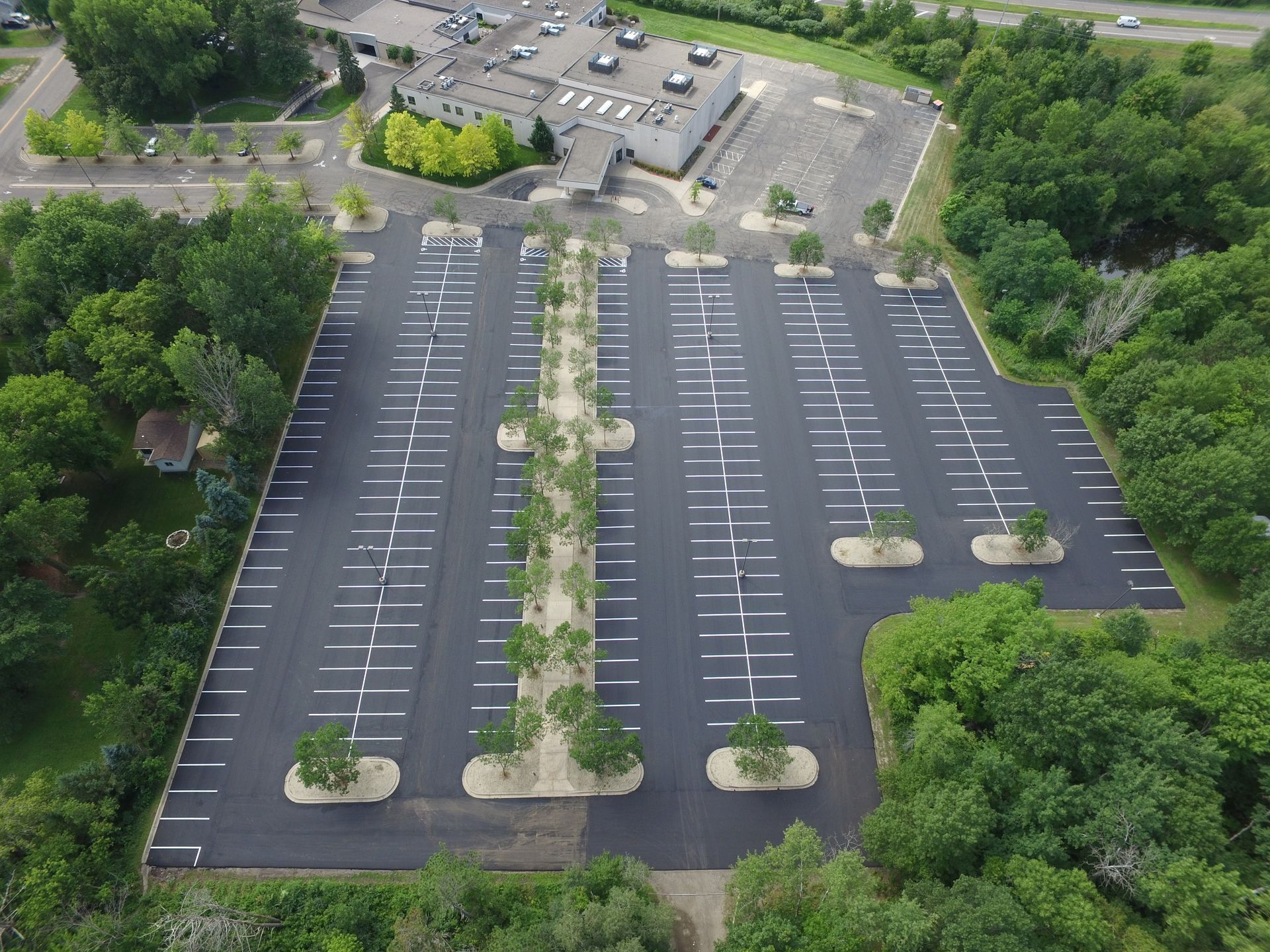 Empty parking lot with painted white spaces and landscaped islands, surrounded by trees.